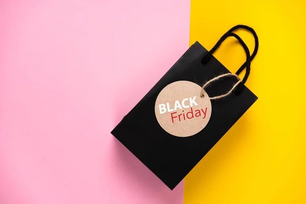 Black gift bag with label on colored background black friday concept. With place for text.