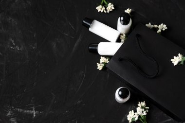 Siyah kese kağıdında kozmetik ürünleri olan küçük kavanozlar ve indirimli çiçekler.