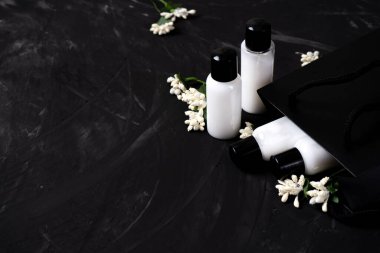 Küçük kavanozlardaki kozmetik seti. Koyu bir arka planda, çiçekli bir kese kağıdında. Kara Cuma.