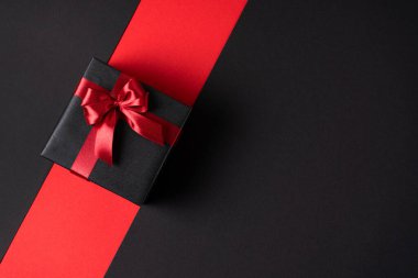 Siyah hediye kutusu, koyu renk zıt bir arka plan, parlak desenli bir fiyonk ile süslenmiş. Üst görünüm