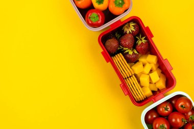 Kurabiyeli beslenme çantaları, peynir parçaları, çilek, domates ve biber sarı arka planda. Okul yemeği ve iş yemeği konsepti. Kopyalama alanı olan üst görünüm
