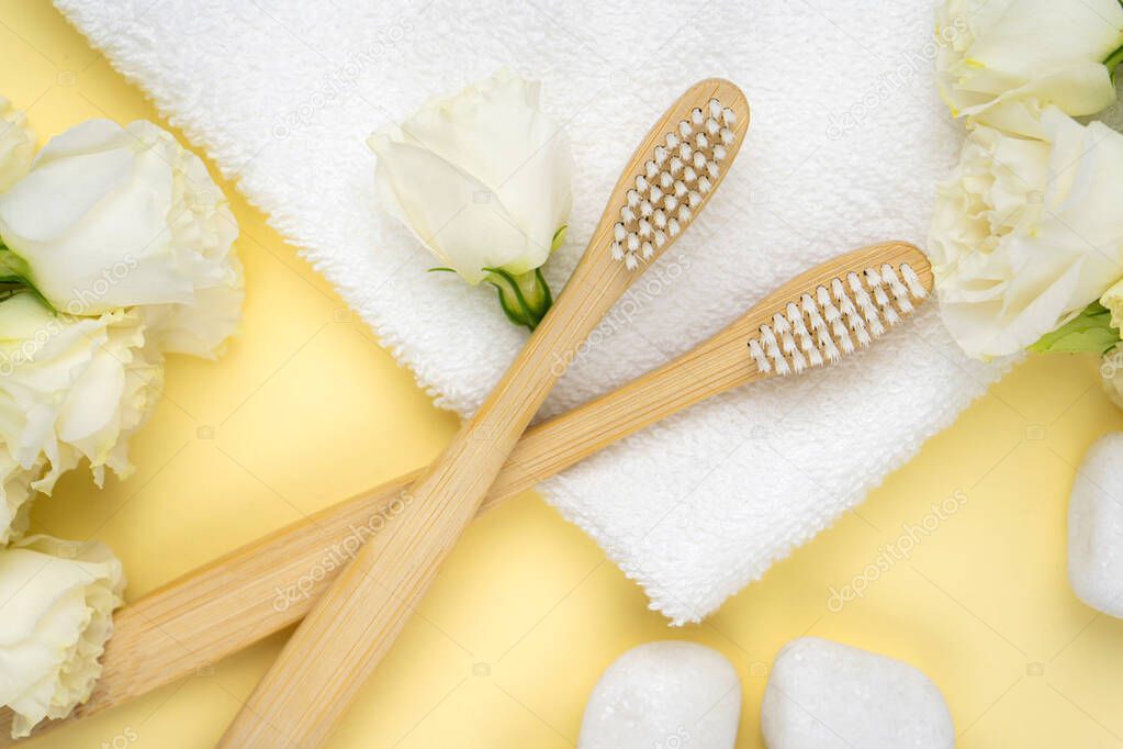 Bamboo toothbrushes with natural white bristles on a towel next to pebbles with a flower on yellow background. The concept of zero waste, modern trends in conscious consumption. Close up