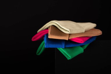 Farklı parlak renklerdeki berelerin bir koleksiyonu, reklam için arka planda koyu bir zıt model üzerine tek tek istiflenmiş. Yan görünüm