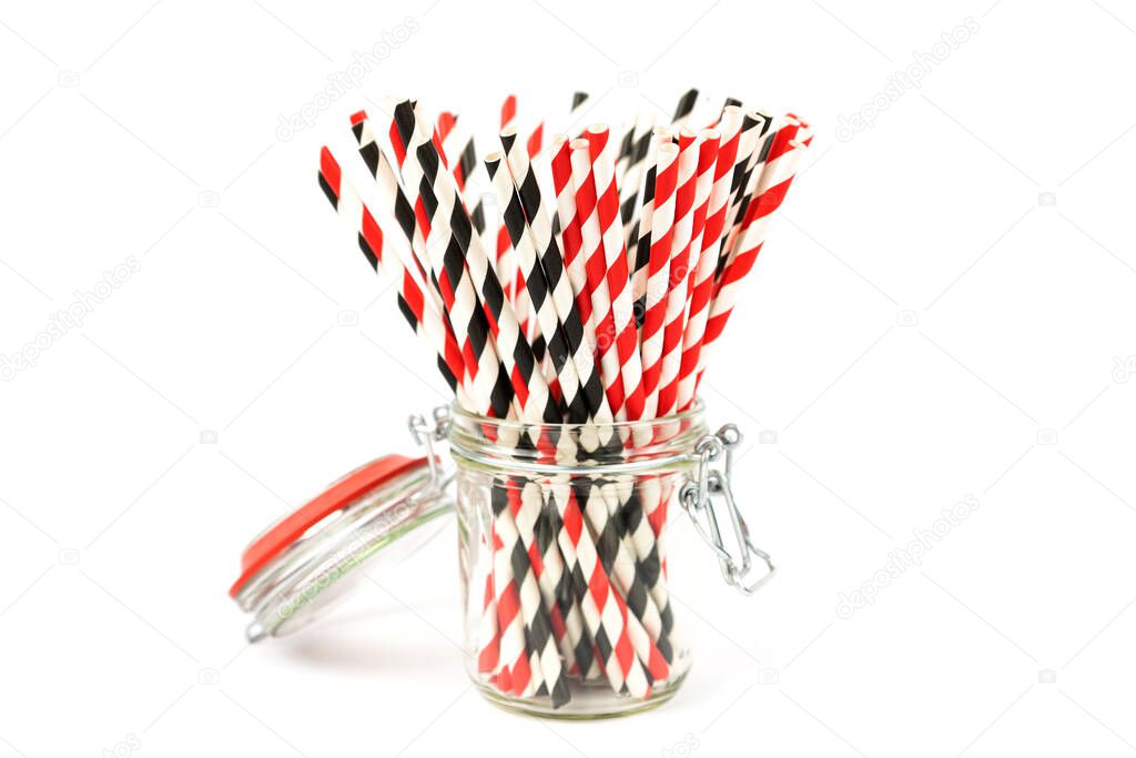 Striped paper cocktail tubes of red and black for drinking juice or cocktail life, in a glass jar with a hermetic lid on a white background. Side view. Holiday concept, no plastic. 