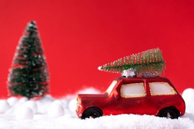 Çatıda ve arka planda çam ağacı olan kırmızı minyatür bir oyuncak araba, karlı parlak kırmızı bir Noel arkaplanı. Noel için konsept, tebrik kartı. Boşluğu kopyala
