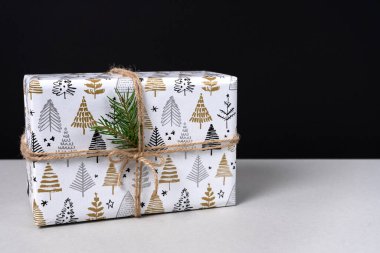 Gri ve siyah arka planda boyanmış Noel ağaçlarıyla kağıda sarılmış Noel hediyesi. Uzayı kopyala Yan görünüm