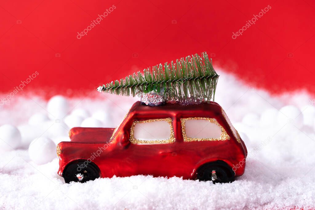 Miniature toy red car with a pine tree on the roof, bright red Christmas background with snow. Concept for Christmas, greeting card. Side view. Close up