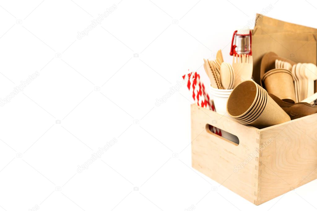 Wooden box with new fast food utensils. Disposable tableware set, wooden cutlery, craft bags, glass bottle and paper cocktail tubes. Side view. Copy space