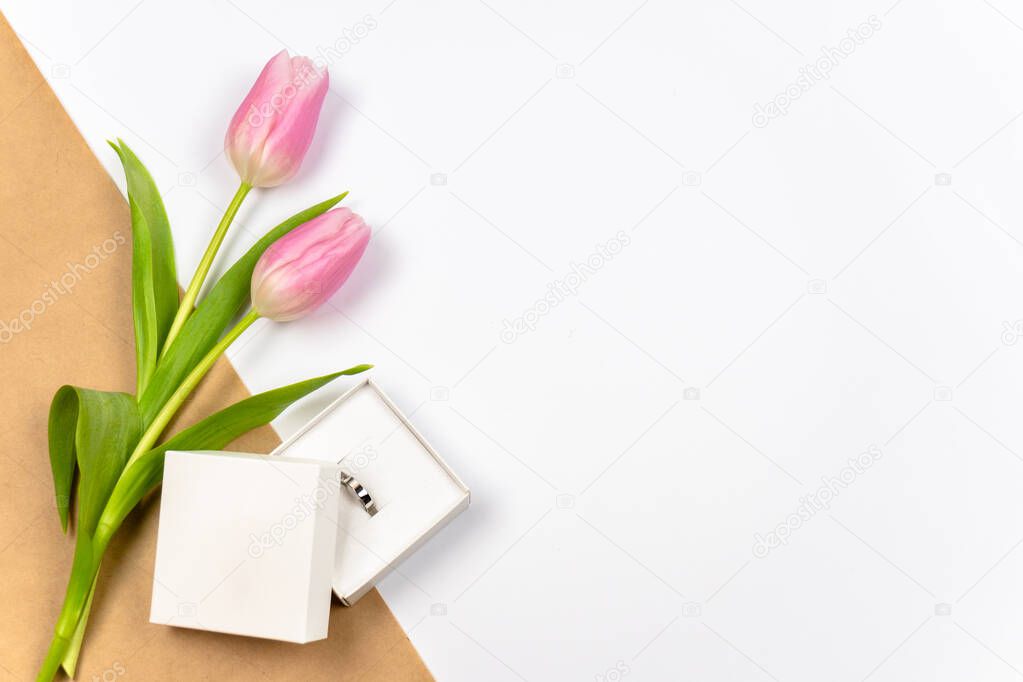 Pink tulips with ring as a gift on white background with crafting paper. Mother's Day, Valentine's Day, Easter. Copy space 