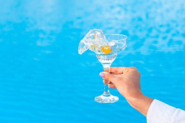 Bir kadın havuzun arka planında sıçramalar olan bir bardak martini sallıyor. Yaz partisi. Boşluğu kopyala
