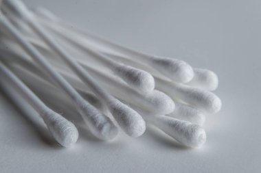 Gri arkaplanda beyaz pamuklu çubuk ya da pamuk tomurcukları var. Kulaklar için beyaz plastik bir tabanda, çapraz