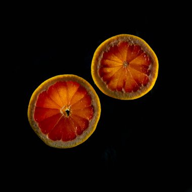 Dilimlenmiş greyfurt. Siyah arka planda yarı izole. Pembe, portakallı taze greyfurt narenciye, zevkle dilimlenmiş, dramatik ışık dokusu, arka planda renkli dilimlenmiş meyveler ışıklandırılmış, kopyalama alanı