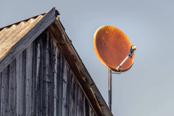 broken and old rusty satellite dish on wooden gable  roof and blue sky background.