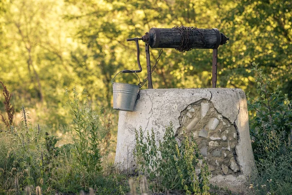 Ancient draw-well in European village, Old Water Well With Pulley and Bucket, Moldova, Green grass and trees. Sunny day. sunset