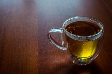 Cam bardaktaki gül yapraklarından taze çay. Koyu kahverengi arka planda pembe sıcak içecek.