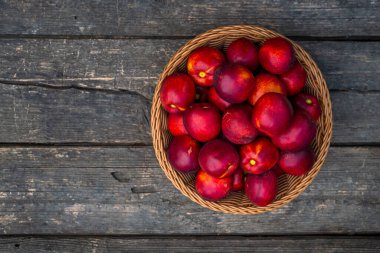 Bir tepsi taze kırmızı nektarin. Ahşap arka plan. Üst manzara taze organik ahşap masa arka plan örülmüş sepet sulu meyve