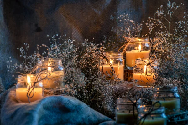 Wax handmade home-based  Burning white candle in the jar coarse textile Vintage  glow Flame dry bouquet gypsophila flower rustic dark mood orange blue light