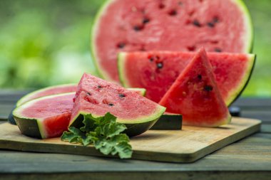 Lezzetli karpuz açık hava ahşap masa, yeşil doğal arka plan dilimleme güneşli gün, hurda, taze olgun kırmızı yaprak, yaz güneşli bahçe suyu organik tatlı meyve, vejetaryen yemeği lezzetli dilimlenmiş tahta tabak