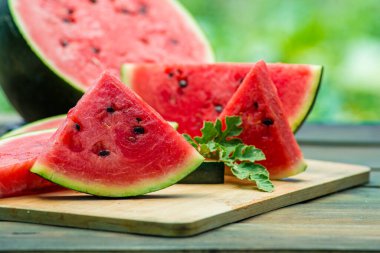 Lezzetli karpuz açık hava ahşap masa, yeşil doğal arka plan dilimleme güneşli gün, hurda, taze olgun kırmızı yaprak, yaz güneşli bahçe suyu organik tatlı meyve, vejetaryen yemeği lezzetli dilimlenmiş tahta tabak