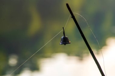 Old Brass Bell on a fishing spinning rod. Fishing feeder on the river. Blurred background