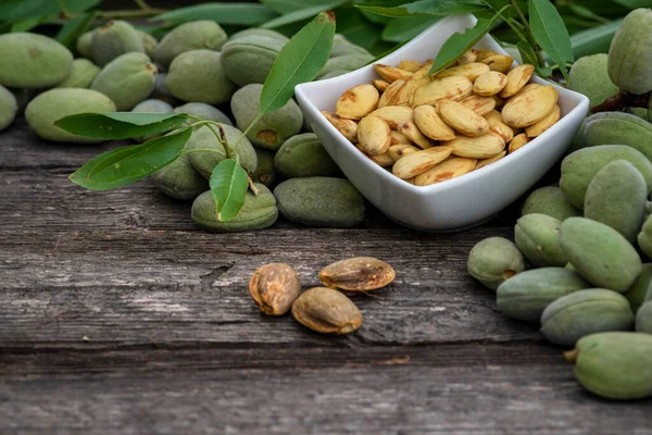 Green almonds background   fresh raw unripe wooden rustic table blurred garden background leaves, Top view concept with copy space shell  tree branch frame without shell  peeling white Bowl