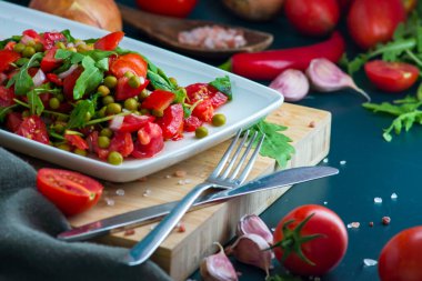 summer salad, tomatoes, green peas, arugula, onion, olive oil, garlic, hot pepper fork knife bamboo cutting board pastel green napkin  textile, salt Vegetarian vegan food