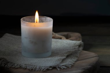 Burning white candle light on old dark wooden table background  burlap sack Halloween Aromatherapy smoke rustic cutting board napkin christmas blue cozy textile