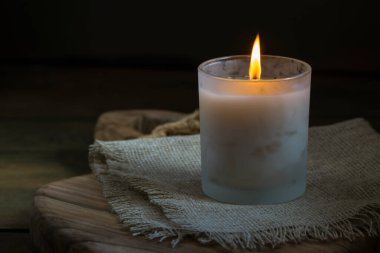 Burning white candle light on old dark wooden table background  burlap sack Halloween Aromatherapy smoke rustic cutting board napkin christmas blue cozy textile