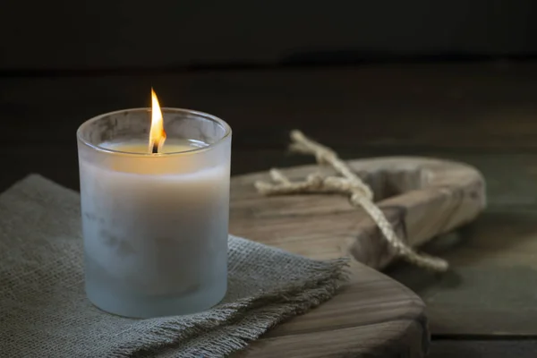 Burning white candle light on old dark wooden table background  burlap sack Halloween Aromatherapy smoke rustic cutting board napkin christmas blue cozy textile