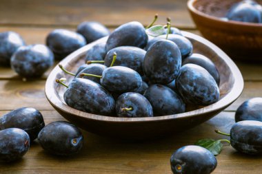 Olgun mavi taze organik tatlı erikler ağaçtan toplanmış, ceviz ağacı kasesi içeride. Sonbahar meyveleri kırsal ahşap kara arka plan yaprak kil hasat