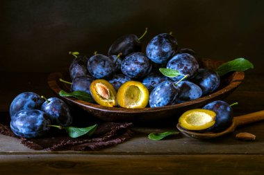 Olgun mavi taze organik tatlı erikler ağaçtan toplanmış, ceviz ağacı kasesi içeride. Sonbahar meyveleri kırsal ahşap kara arka plan yaprak kil hasat