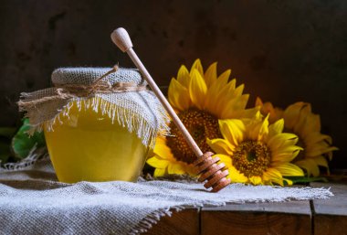 Şeffaf bir kavanozda şeffaf ayçiçeği balı, çuval peçete kapağı kapağı, sağlıklı beslenme konsepti, eski ahşap arka plan çömleği, hala koyu yiyecek cam kasesi.