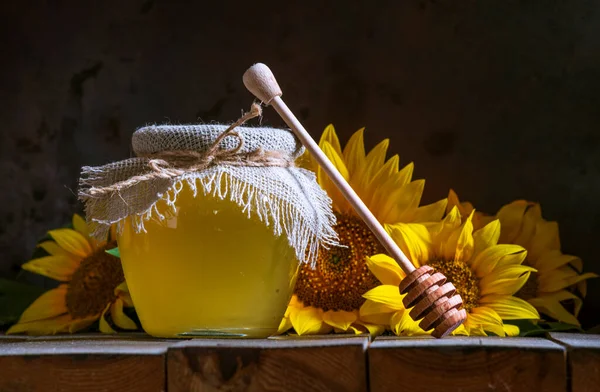 Şeffaf bir kavanozda şeffaf ayçiçeği balı, çuval peçete kapağı kapağı, sağlıklı beslenme konsepti, eski ahşap arka plan çömleği, hala koyu yiyecek cam kasesi.