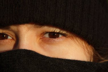 Yüzü atkı ve siyah şapkayla kaplı bir kızın gözleri.