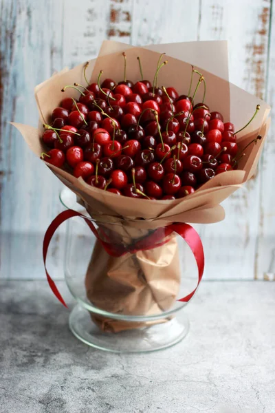 Bright edible round bouquet of cherry berries on the base, wrapped in gold film and tied with a ribbon as an unusual gift. Foodfloristics. Selective focus. — Stock Photo, Image