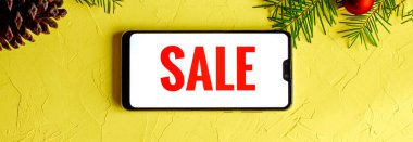 Siyah bir cep telefonunun beyaz arka planında, sarı bir zemin ve köknar dalları ve toplarının yeni yıl dekorunda yatan İngilizce yazılar. Pankart.