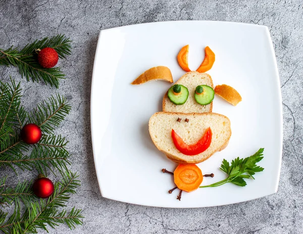 A happy bull riding on a white plate made of white bread, carrots, cucumbers, parsley as a Breakfast decoration for a child for Christmas and New year on a gray concrete background. — Stock Photo, Image