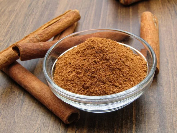 Cinnamon powder in a bowl with Cinnamon sticks on wooden background