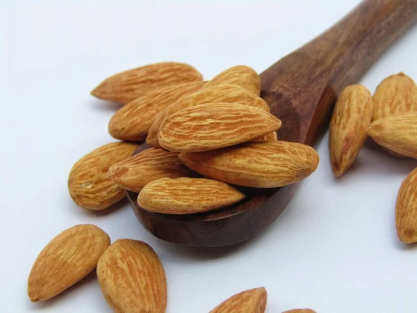 Beyaz arka planda tahta kaşıkta badem. 