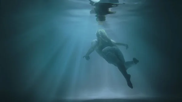 Een meisje drijft onder water tegen een achtergrond van zonneschijn — Stockfoto