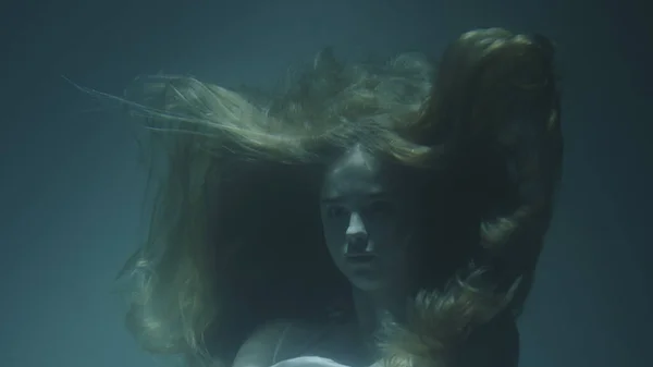 Közelkép egy gyönyörű lányról, vörös hajjal, fehér ruhában, befagyva a víz alatt. — Stock Fotó