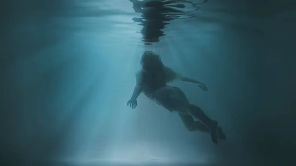 Una chica flota a la superficie bajo el agua sobre un fondo de sol — Foto de Stock