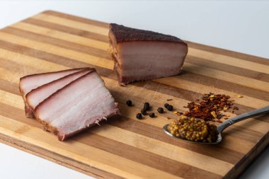 Tütsülenmiş domuz yağı, domuz pastırması, yarım dilim, ahşap bir arka planda. Domuz yağı. Korunmuş domuz eti.