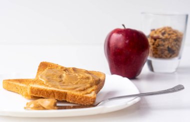 Kahvaltıda fıstık ezmeli sandviç, granola ve elma. Beyaz arka planda fıstık ezmeli tost..