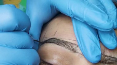 Master makes permanent eyebrow makeup procedure using special needle tattoo machine to woman. Microblading brows tattooing. Dark pigment is ingected under skin.