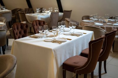 Şık ve zarif, altın kaplama çatal bıçak takımı ve beyaz tabaklar, boş tabaklar. Güzel koltuklar ve tamamen örtülü bir masa..