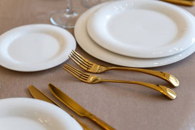 Chic and elegant, gold-plated cutlery and white plates, table setting with empty plates. Clouse-up.