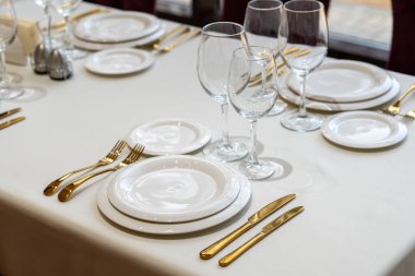 Chic and elegant, gold-plated cutlery and white plates, table setting with empty plates. Clouse-up.