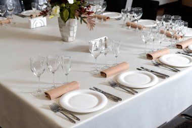 Close up new white porcelain tableware plates on white tablecloths and empty wine glasses ready for dinner.