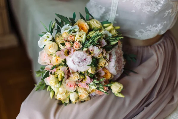 Kytice leží na klíně nevěsty, pivoňky a růže. — Stock fotografie